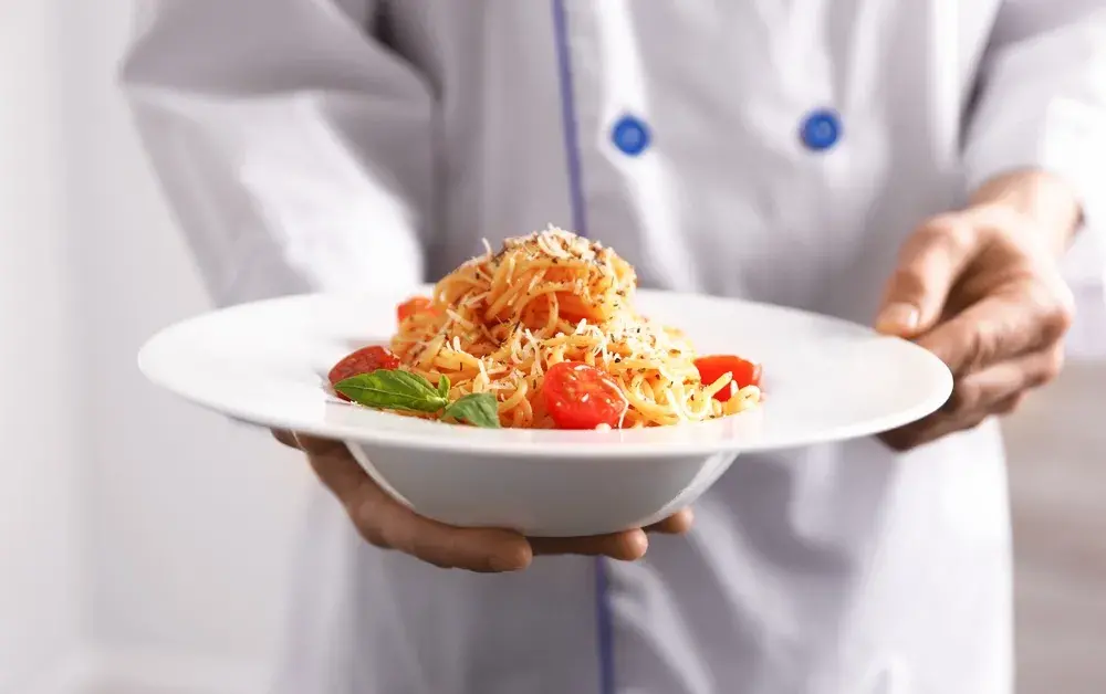 Chef holding spaghetti with cherry tomatoes and basil